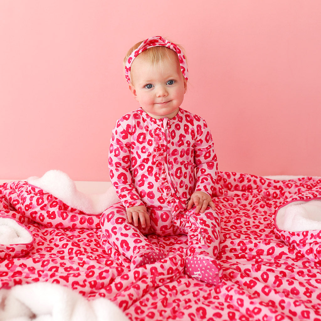 baby wearing pink print onesie and headband sitting on matching blanket