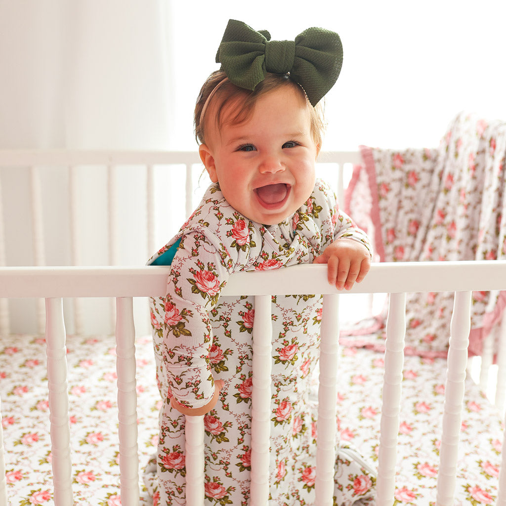 infant standing in crib wearing sleep sack
