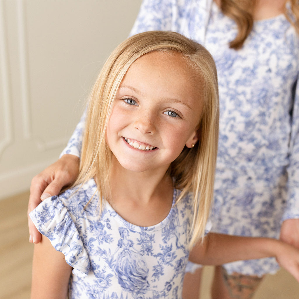 girl posing with mother in background wearing matching blue and white floral print outfits