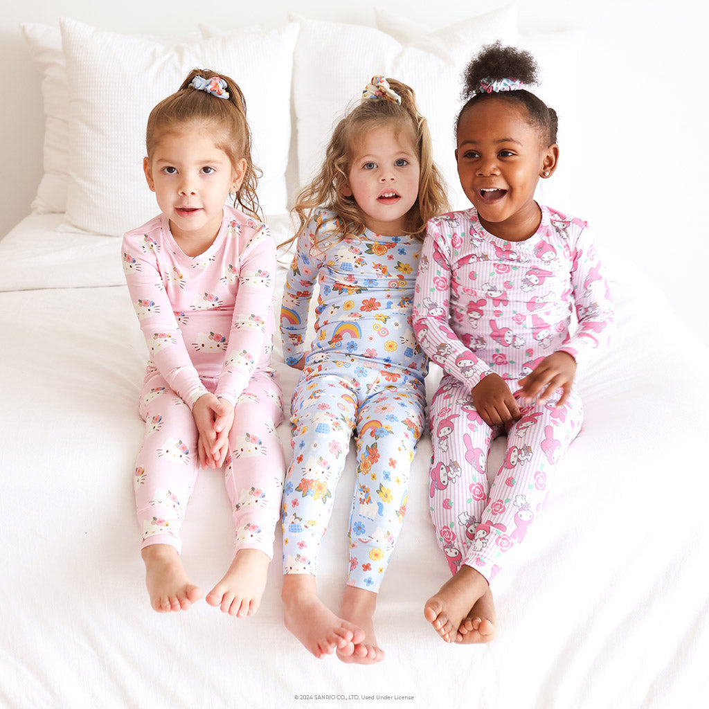 three girls sitting next to one another on bed wearing matching Hello Kitty pajamas