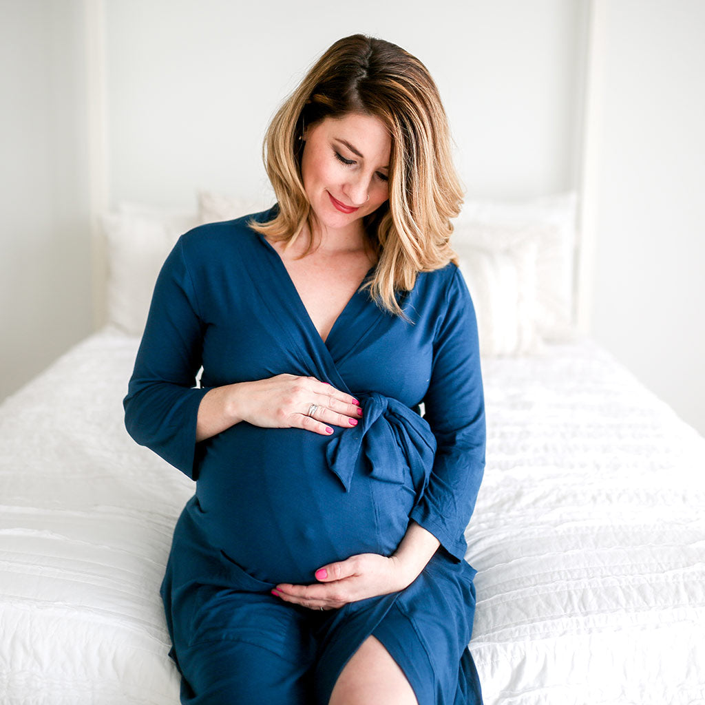 Woman sitting on bed holding baby bump in blue posh peanut maternity robe