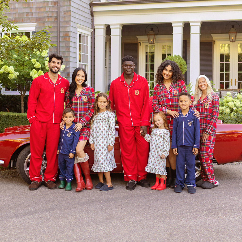 family of nine wearing various christmas themed pajamas standing in front of red car