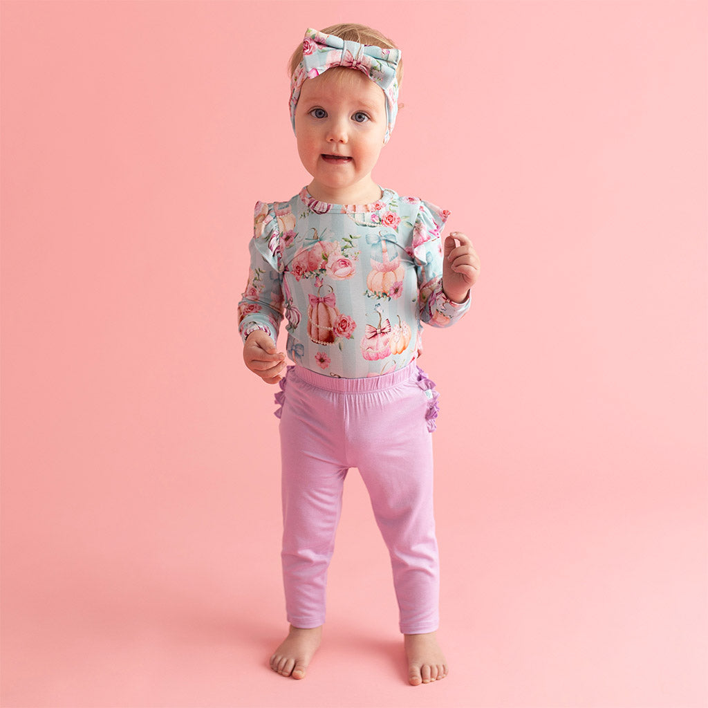 toddler girl standing with whimsy print ruffled top and pink leggings