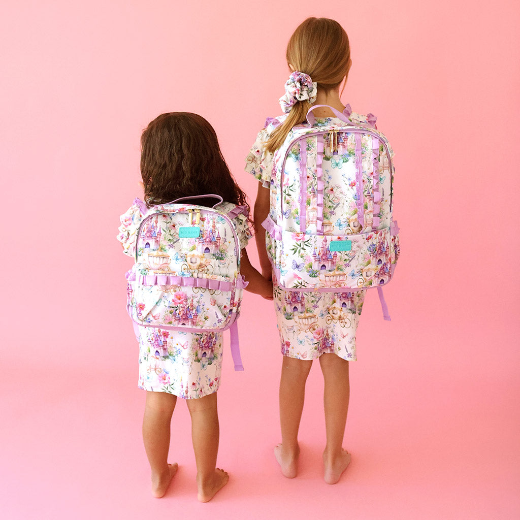 two girls standing together holding hands wearing matching floral whimsy outfits and backpacks