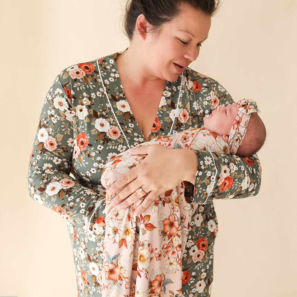 mother wearing floral print robe holding newborn wrapped in swaddle and headband