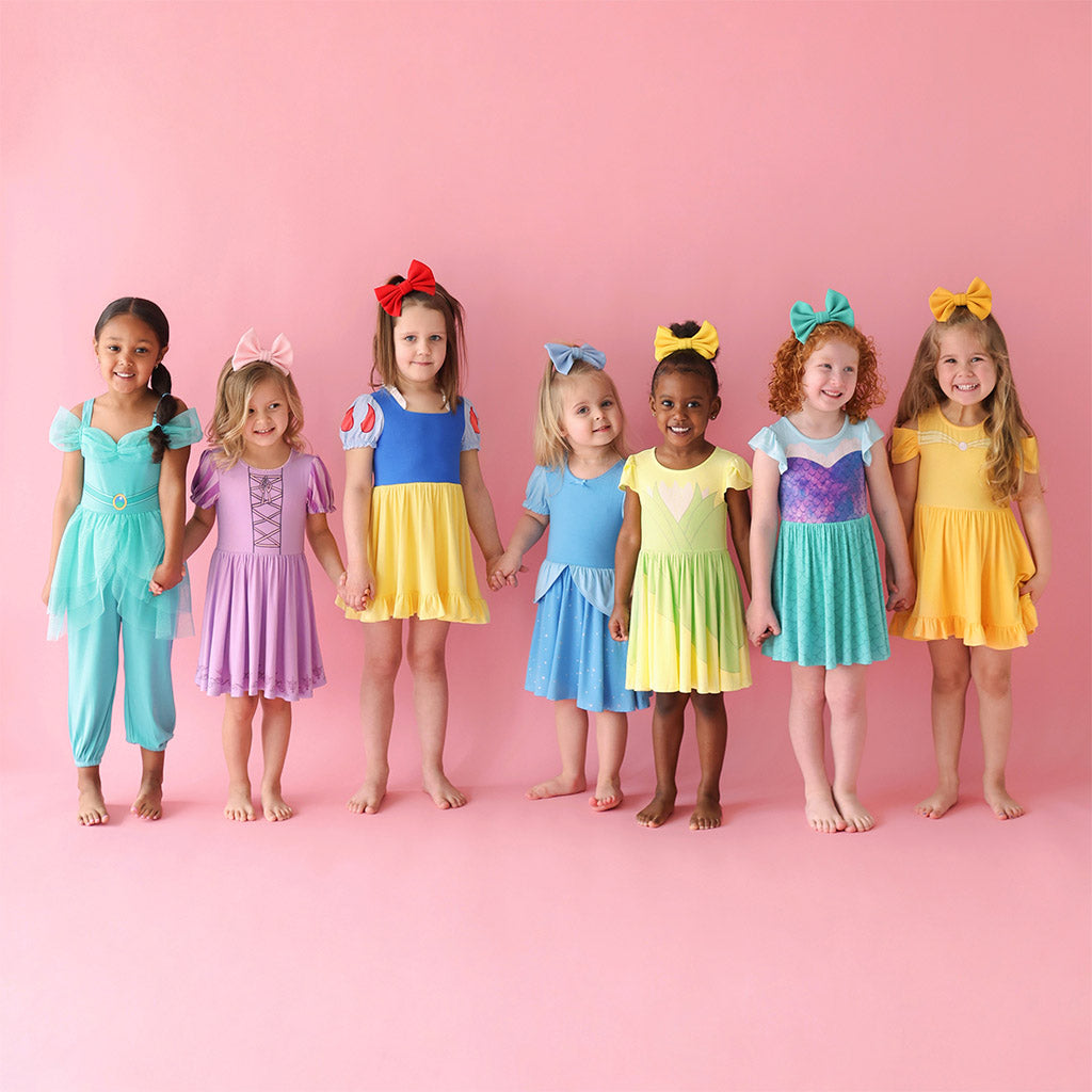 Seven girls holding hands wearing various Disney themed dresses