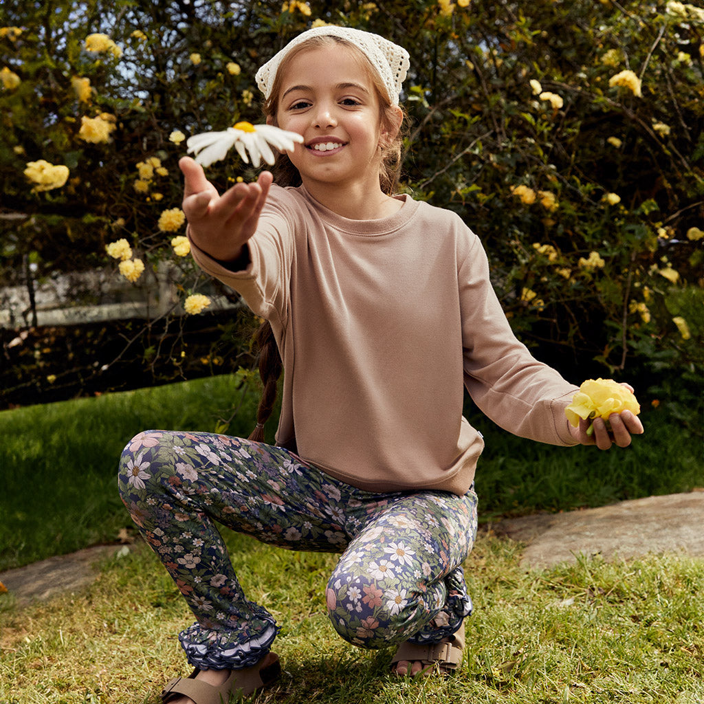 young girl holding flowers in garden wearing floral print leggings