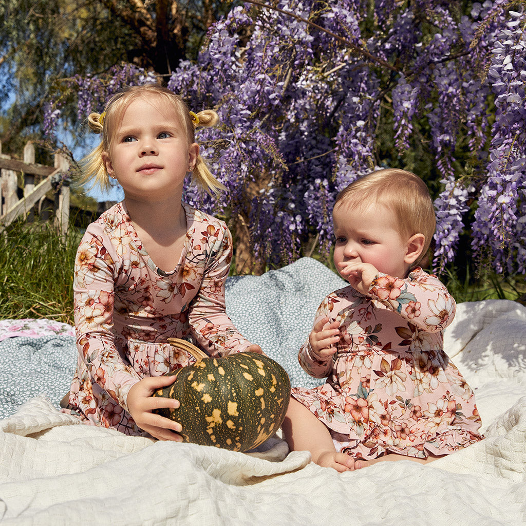 two children sitting in outdoor garden on blanket wearing matching floral outfits