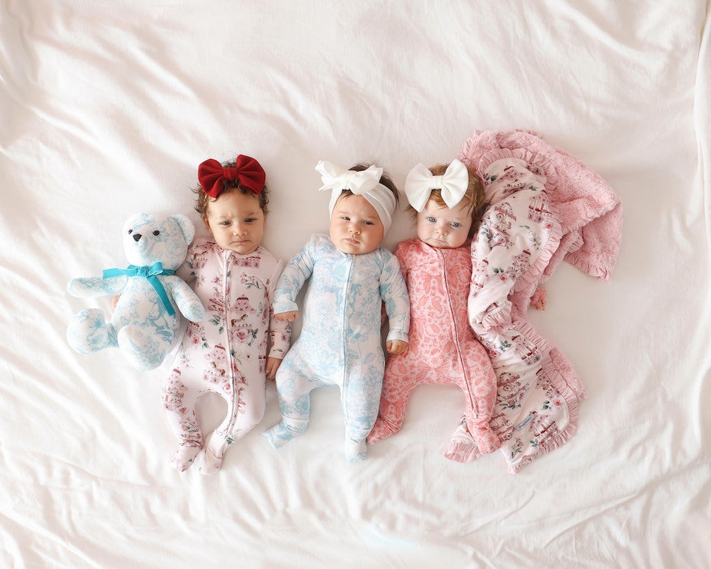 three infants lying next to one another on a bed wearing different whimsy floral print onesies