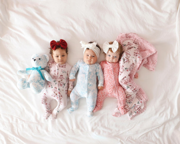 three infants lying next to one another on a bed wearing different whimsy floral print onesies