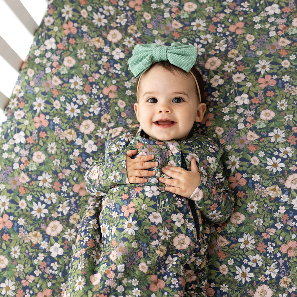 infant laying in crib wearing sleep sack with floral print with matching crib sheet