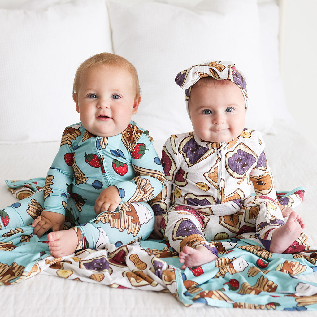 two infants sitting next to one another wearing food themed print onesies