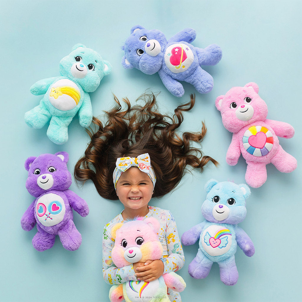 child wearing Care Bears print outfit surrounded by Care Bears plushies of different colors