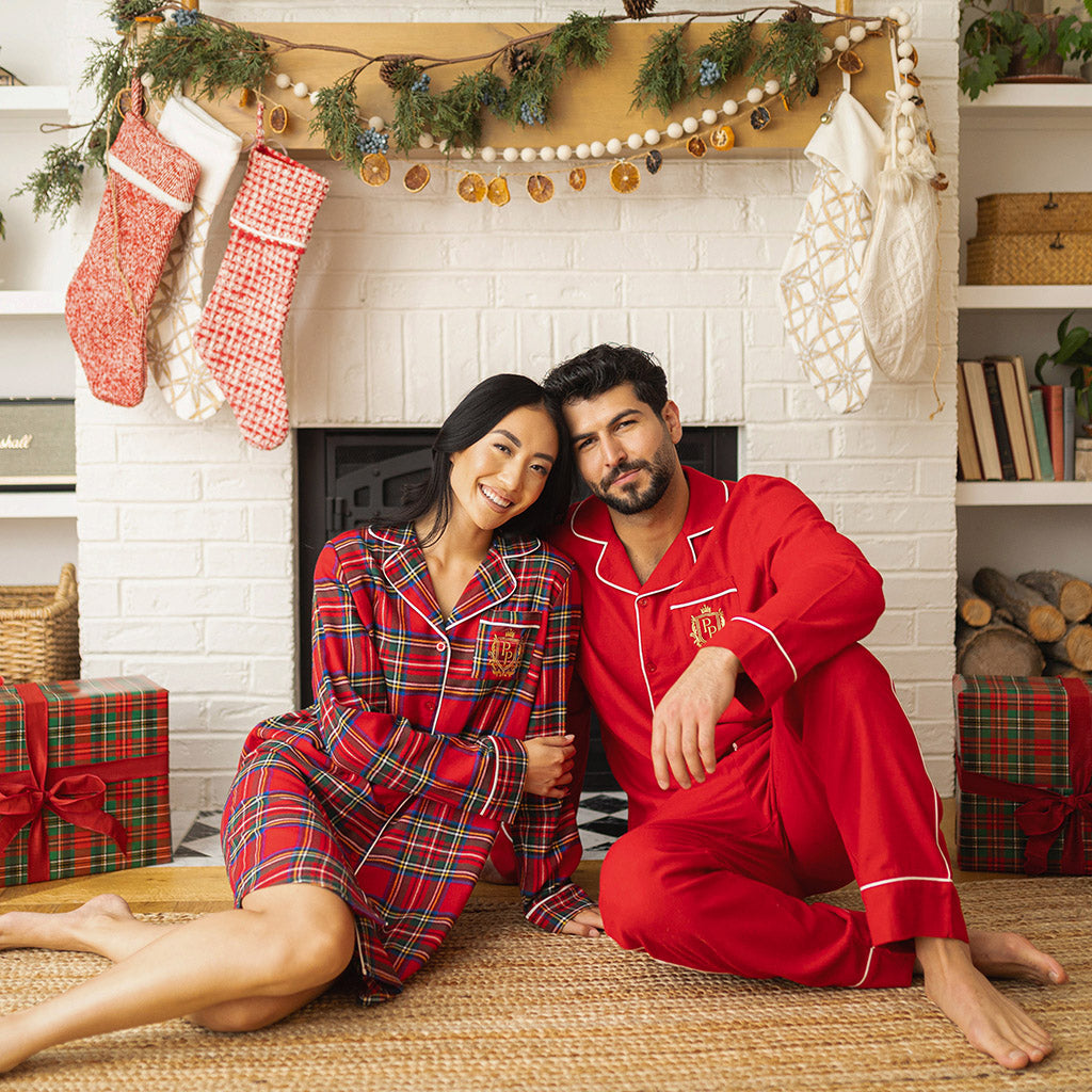 man and woman couple sitting by fireplace wearing matching holiday pajamas