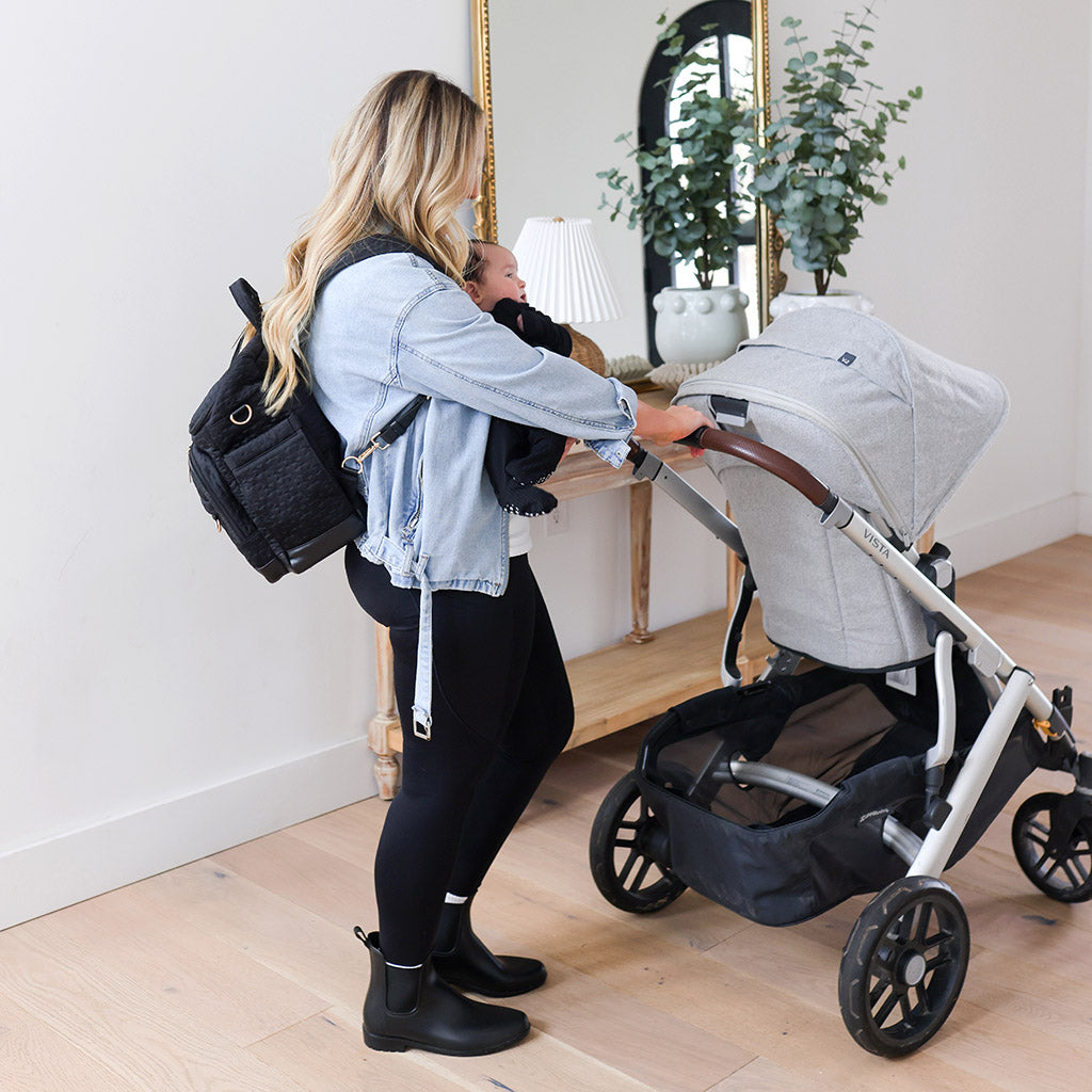 Mother holding baby and pushing stroller leaving house