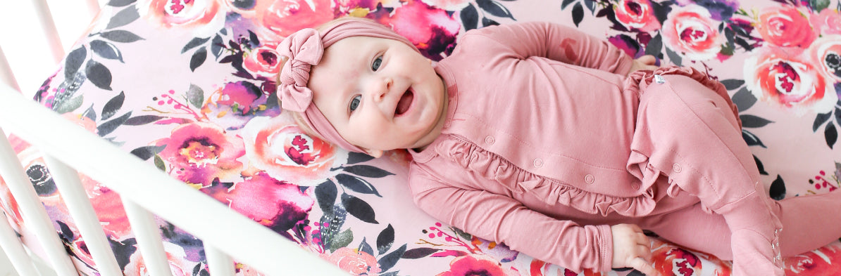 baby girl on top of floral baby crib sheets