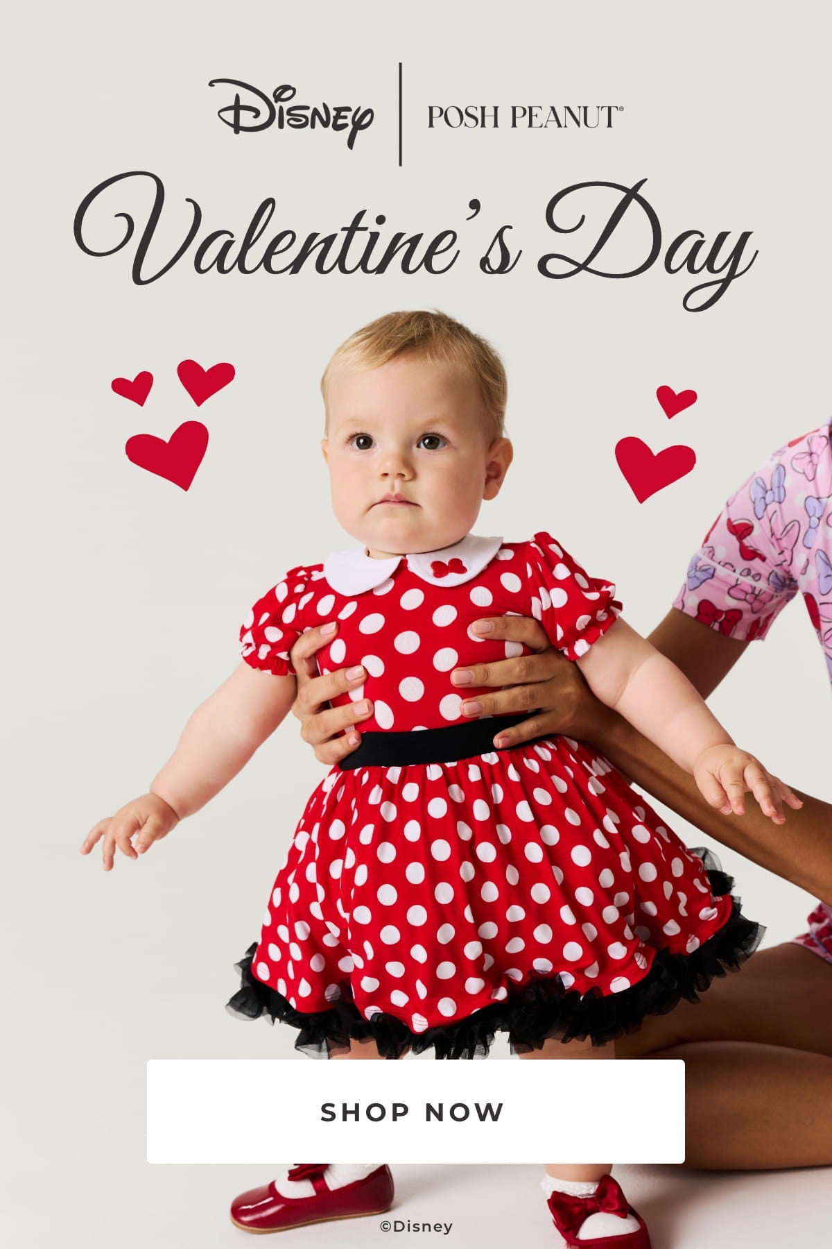 infant girl standing wearing Disney themed red and white dot twirl dress held up with mother's hands with text 'Disney | Posh Peanut® Valentine's Day Shop Now ©Disney' on grey background with red hear graphic elements