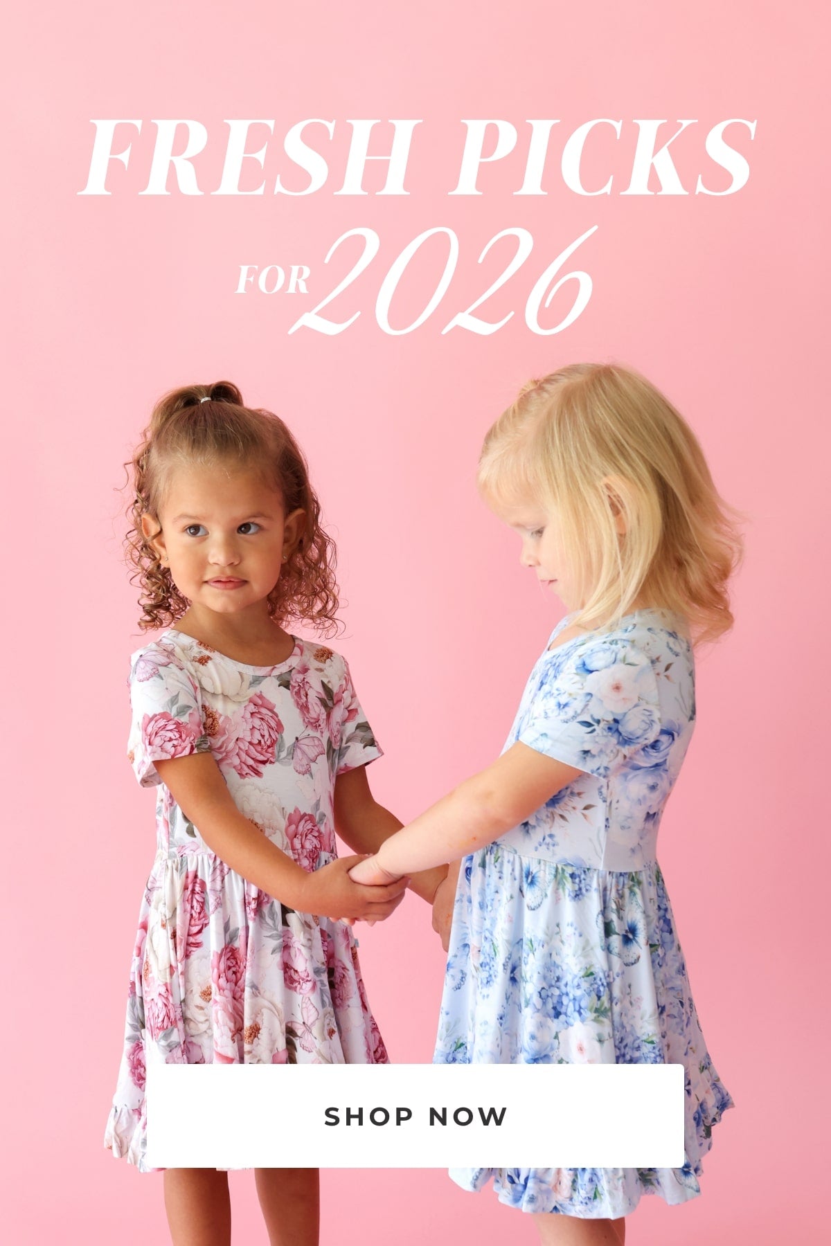 two young girls wearing pink and blue floral themed print twirl dresses holding hands with text 'Fresh Picks for 2026 Shop Now' on pink background