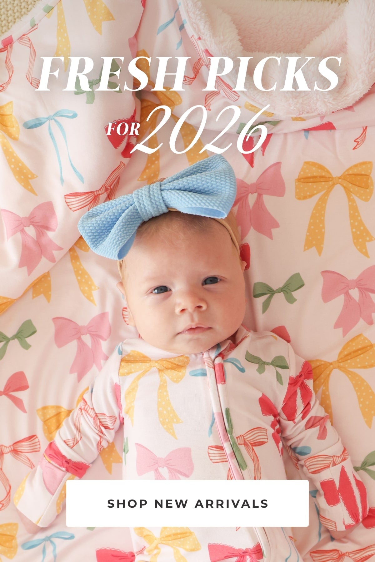 Baby wearing a blue bow lying on a colorful bow-patterned blanket with text 'Fresh Picks for 2026' and 'Shop New Arrivals'.