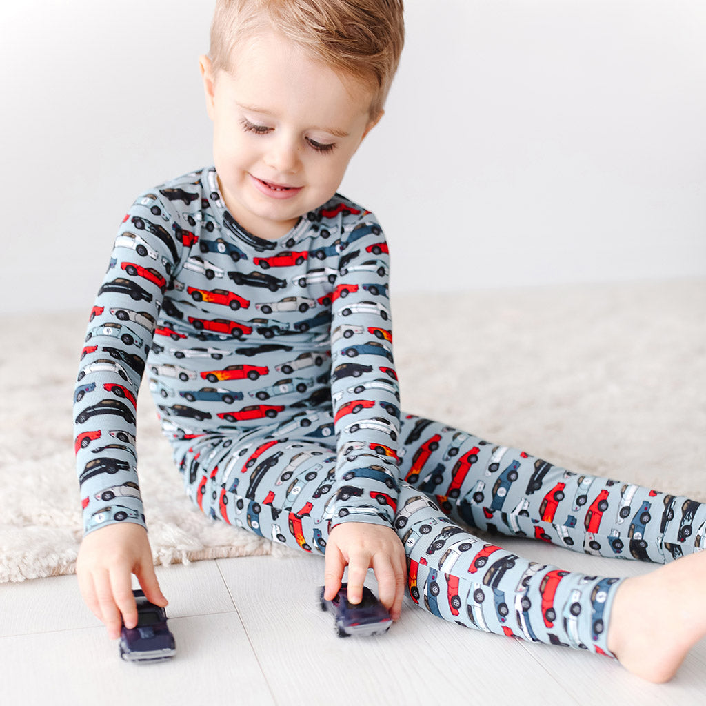 Child wearing a car-patterned pajama set sitting on a white floor.