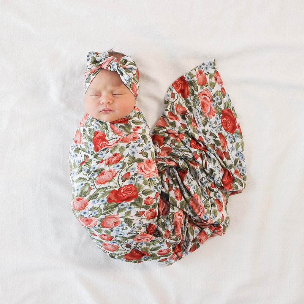 Newborn baby wrapped in a floral swaddle blanket with matching headband on a white background