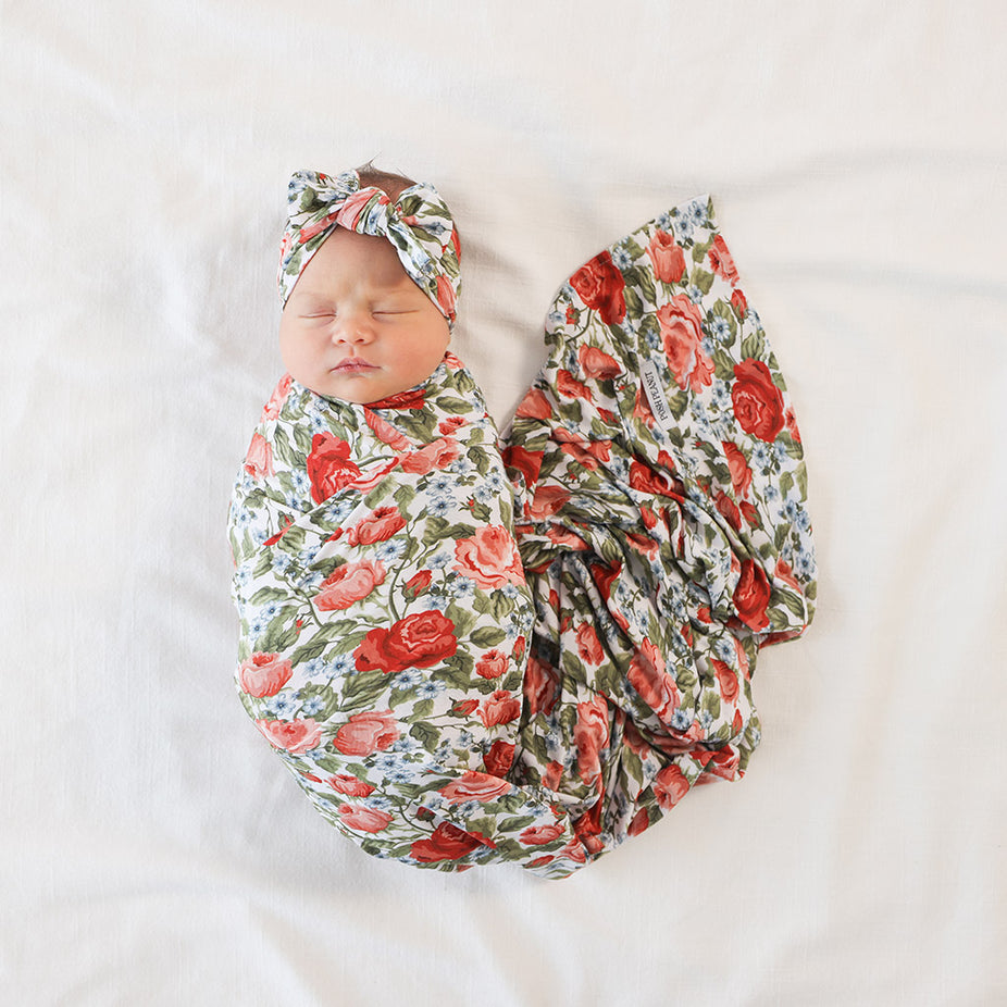 Newborn baby wrapped in a floral swaddle blanket with matching headband on a white background