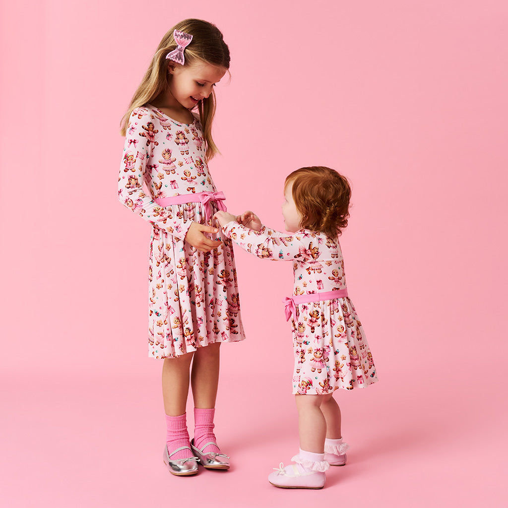 Two young girls in matching floral dresses standing on a pink background