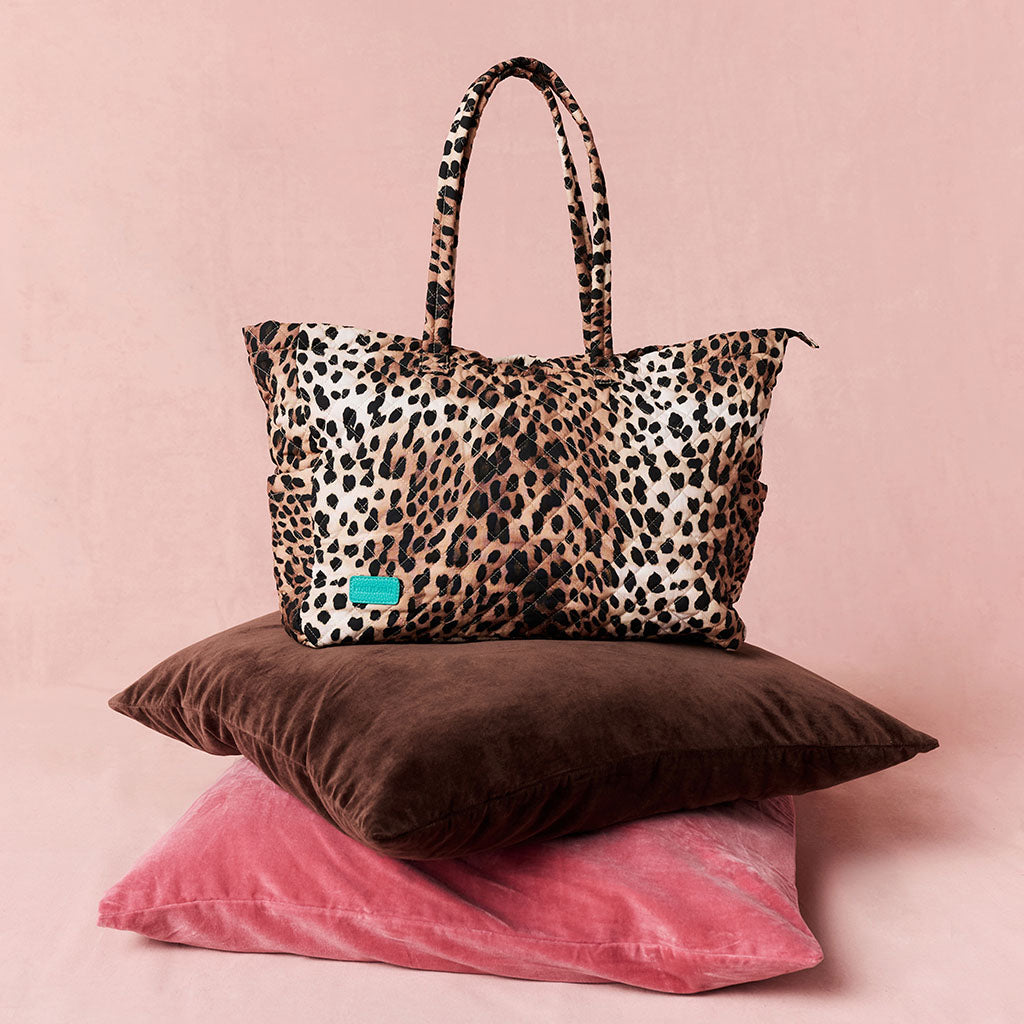 Leopard print tote bag on a pink background with pillows underneath