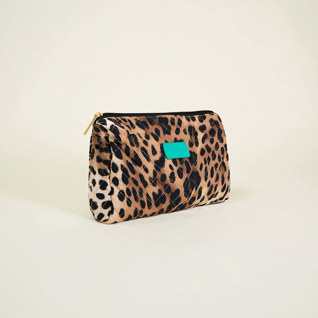 Leopard print toiletries pouch with a turquoise tag on a beige background