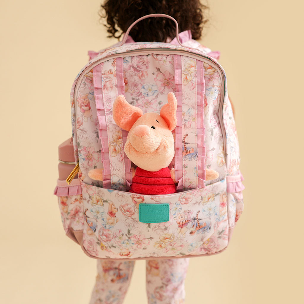 Child with a floral backpack featuring a plush Piglet toy on a beige background
