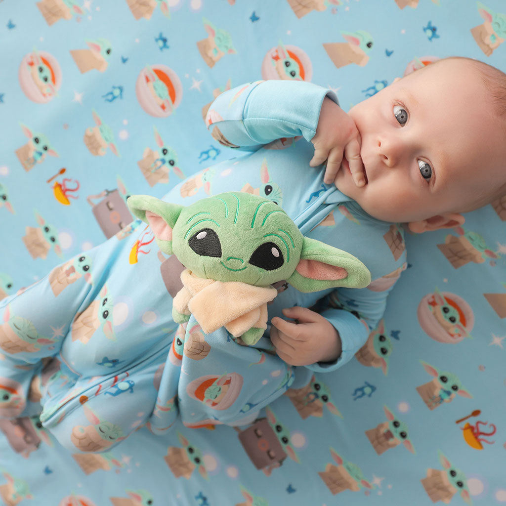 Baby lying on a colorful blanket holding a Star Wars Grogu plush lovey.
