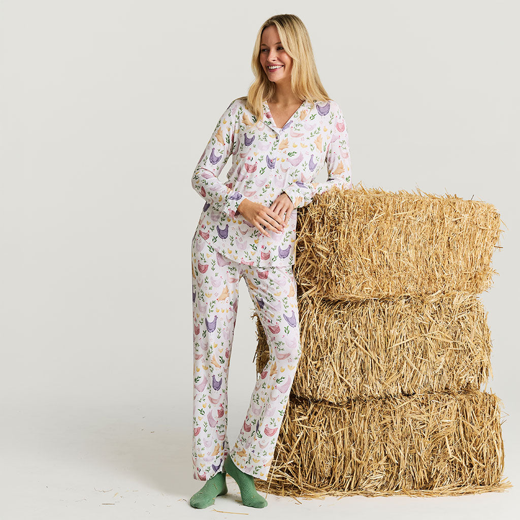 Woman wearing a chicken-patterned pajama set standing next to hay bales on a white background