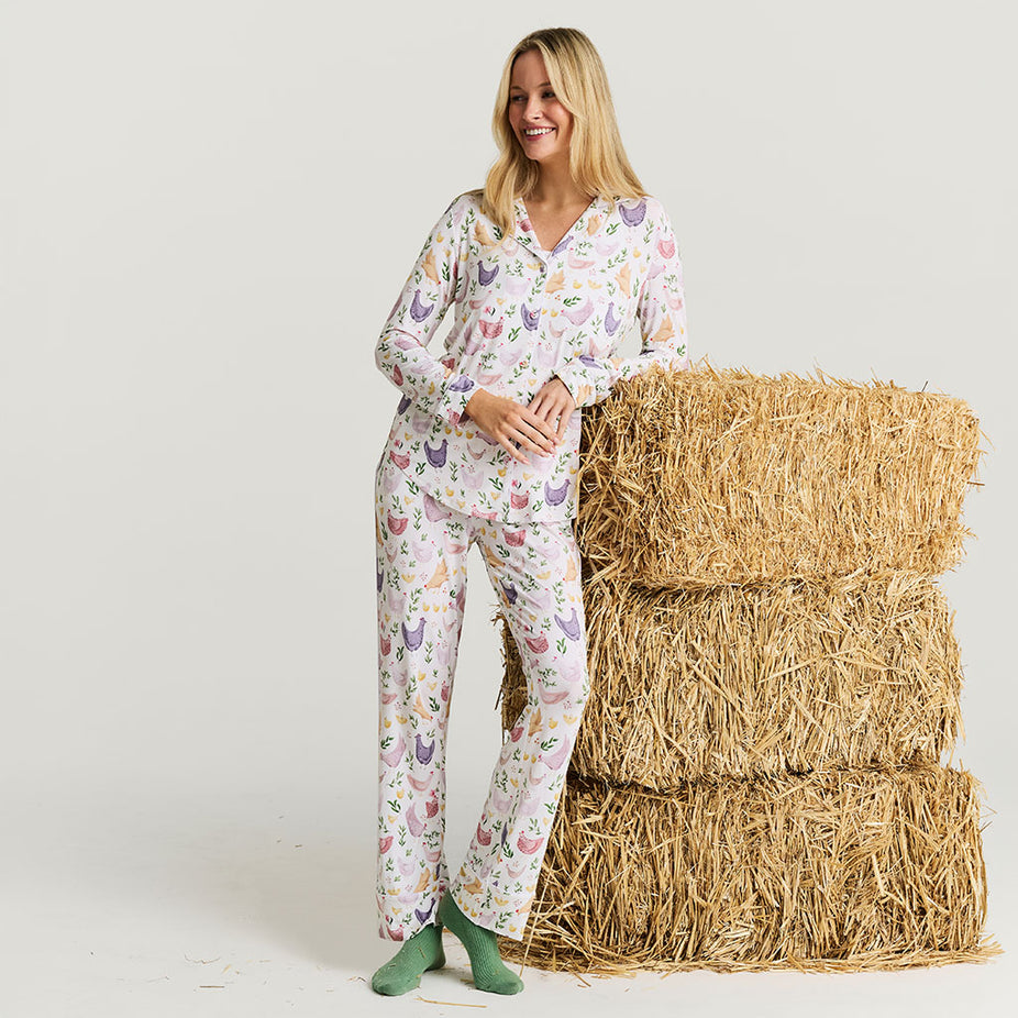 Woman wearing a chicken-patterned pajama set standing next to hay bales on a white background