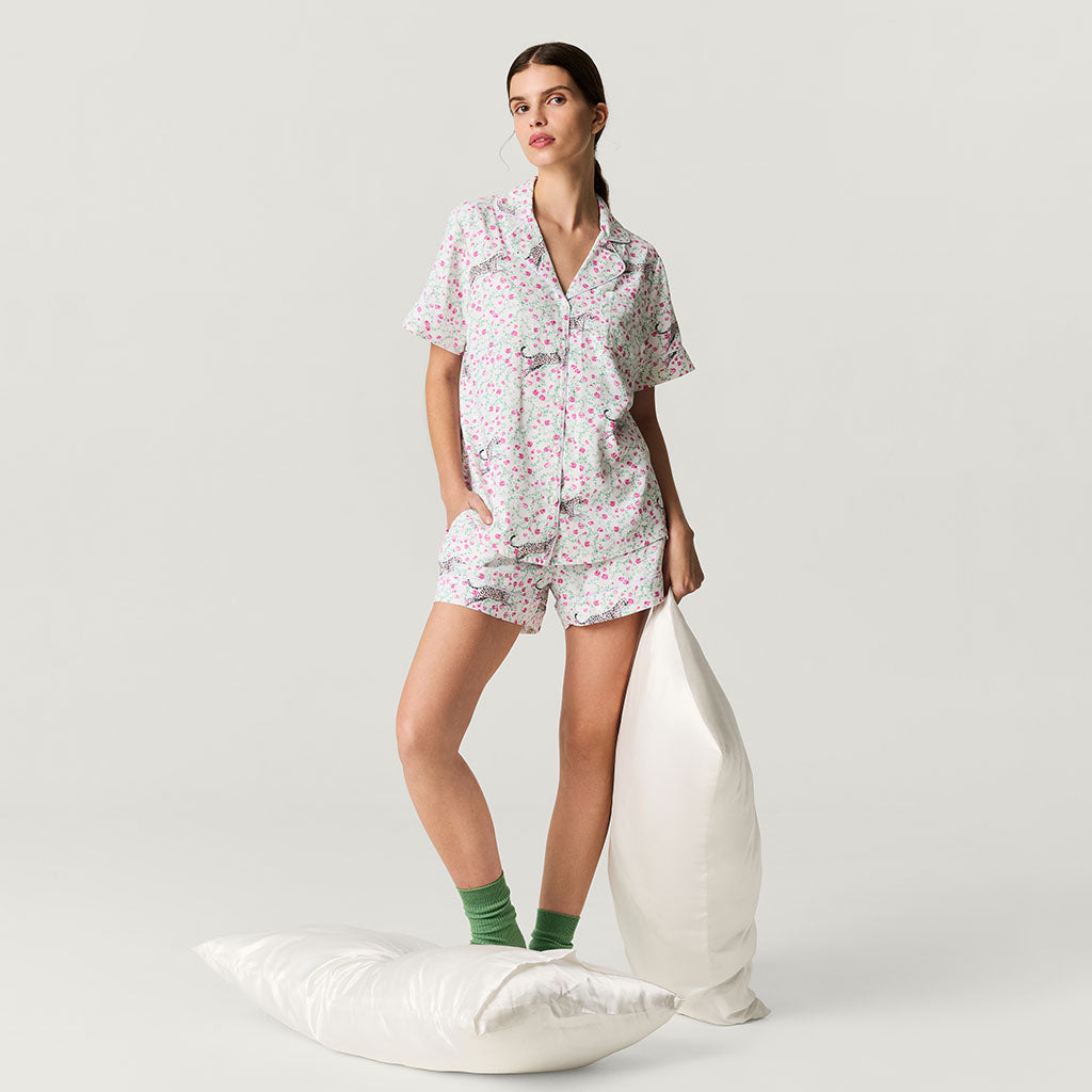 Woman wearing a floral pajama set standing between two pillows on a plain background