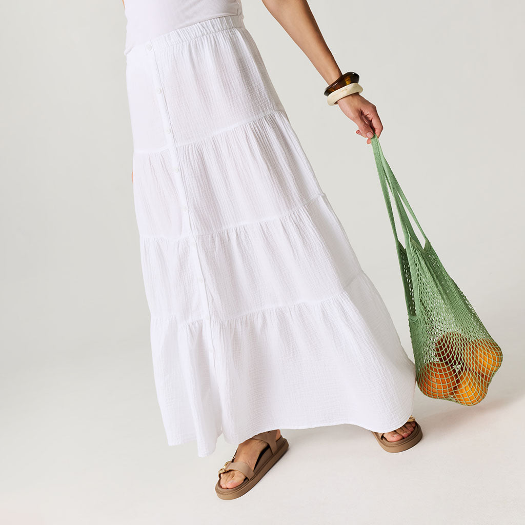 Person holding a green reusable bag with fruits against a plain background