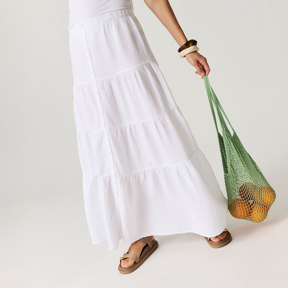 Person holding a green reusable bag with fruits against a plain background