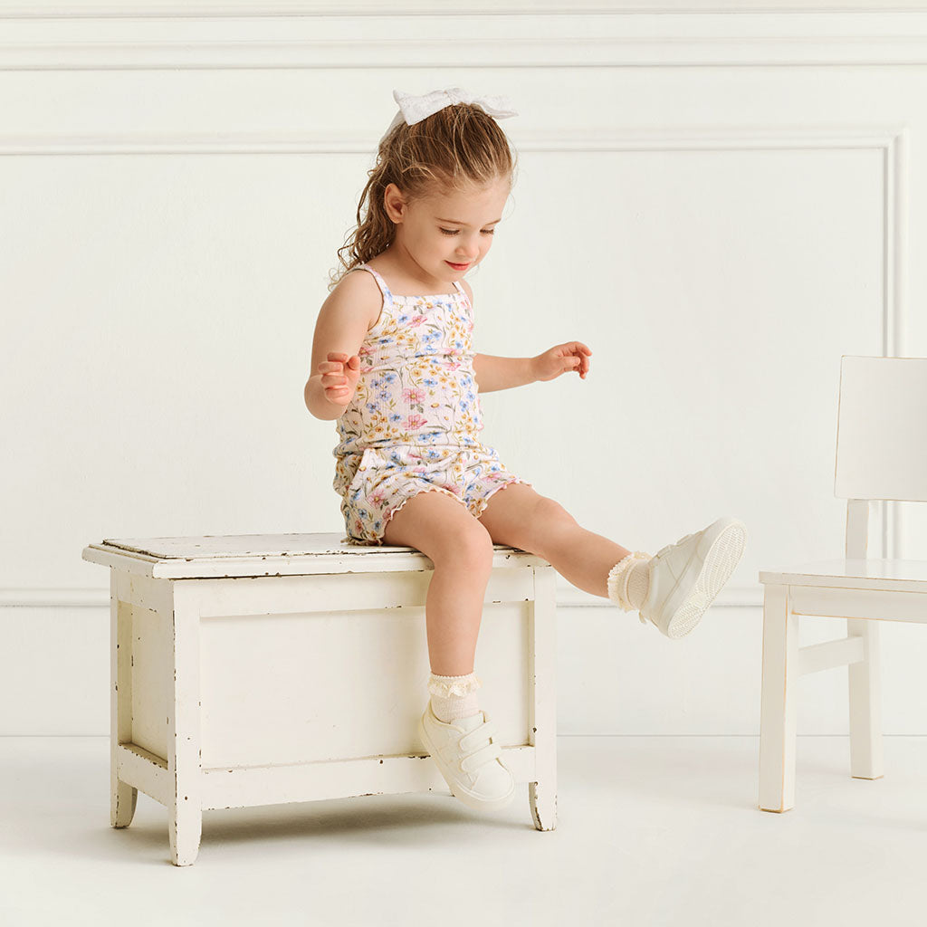 Child sitting, wearing the Posh Peanut Hazel Pointelle Lettuce Edge Cami Short Set, white background