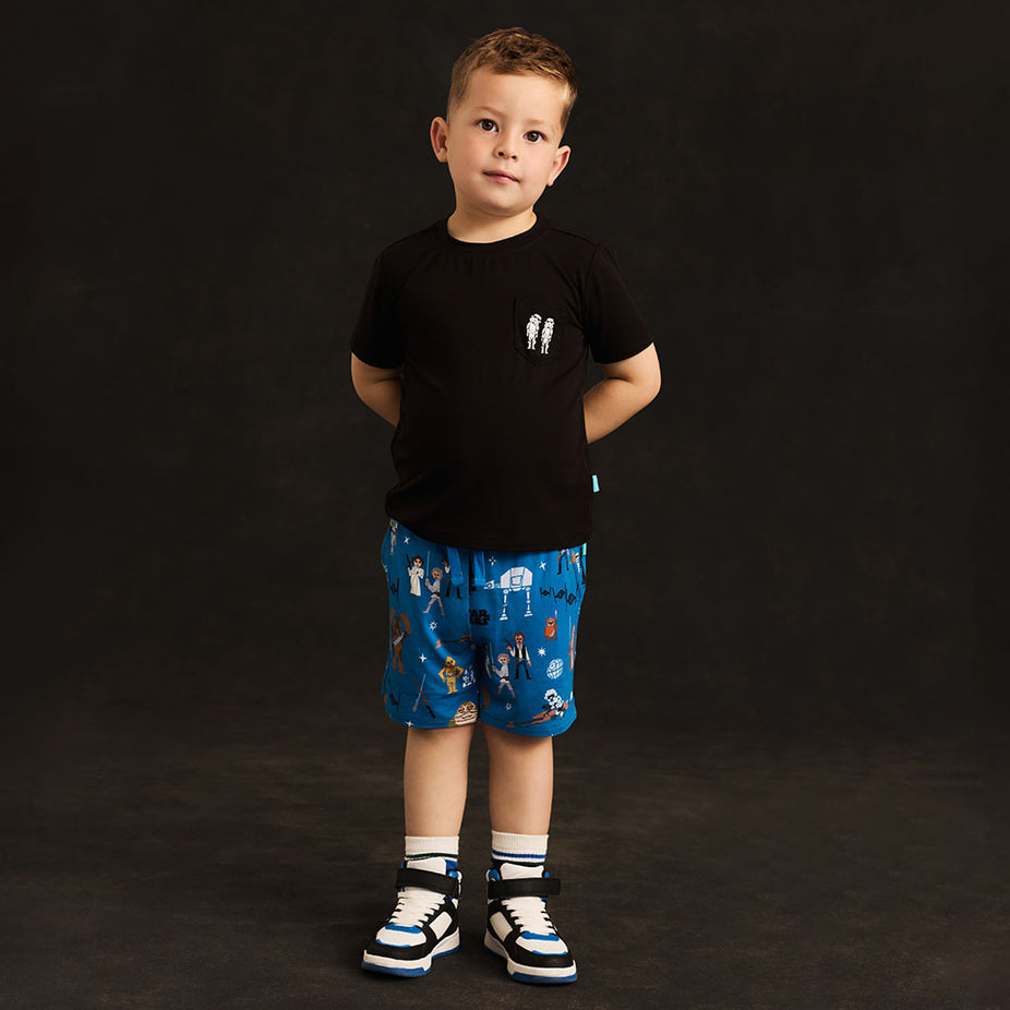 Boy wearing a black tee and blue shorts with Star Wars print against a black background.