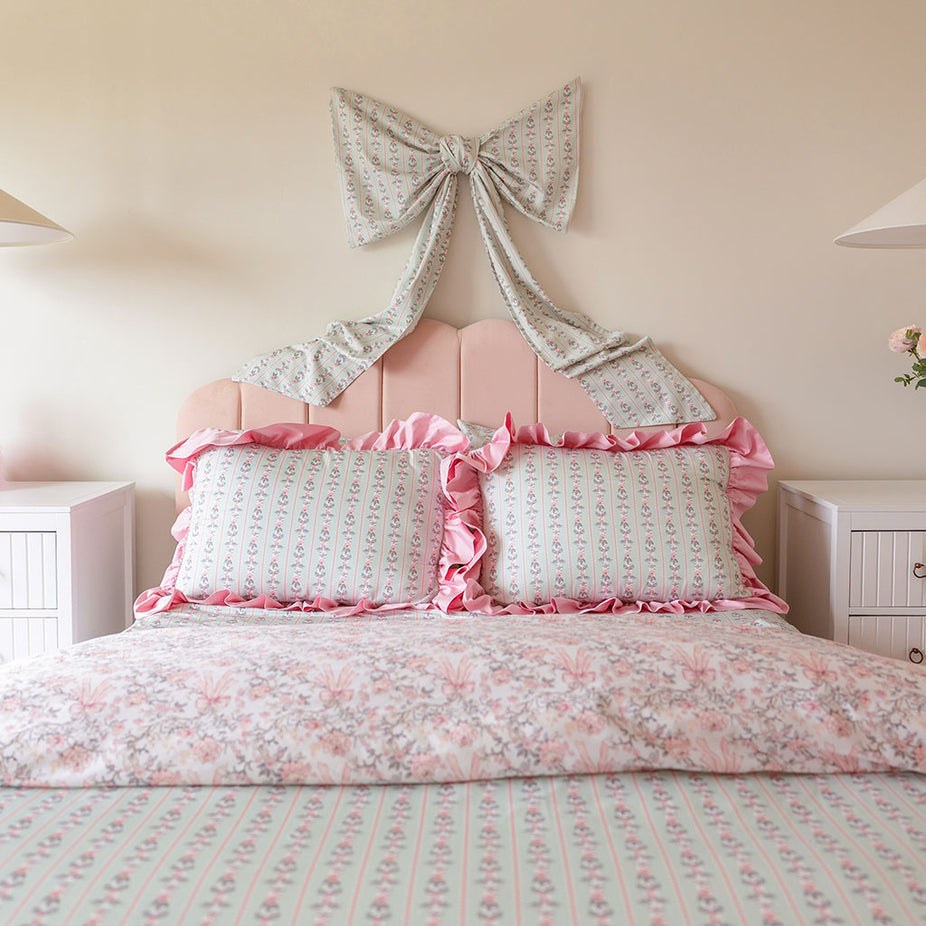 Bed with pink floral bedding and decorative pillows against a light wall.
