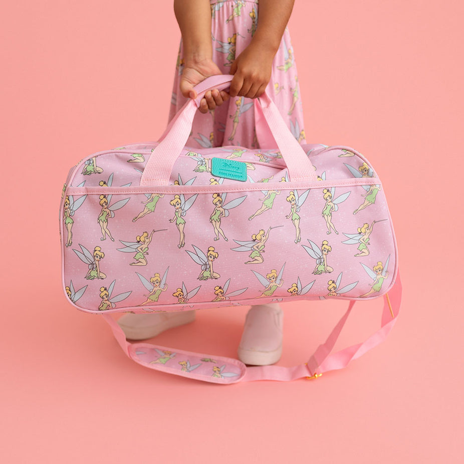 Pink duffel bag with fairy pattern held by a person on a pink background
