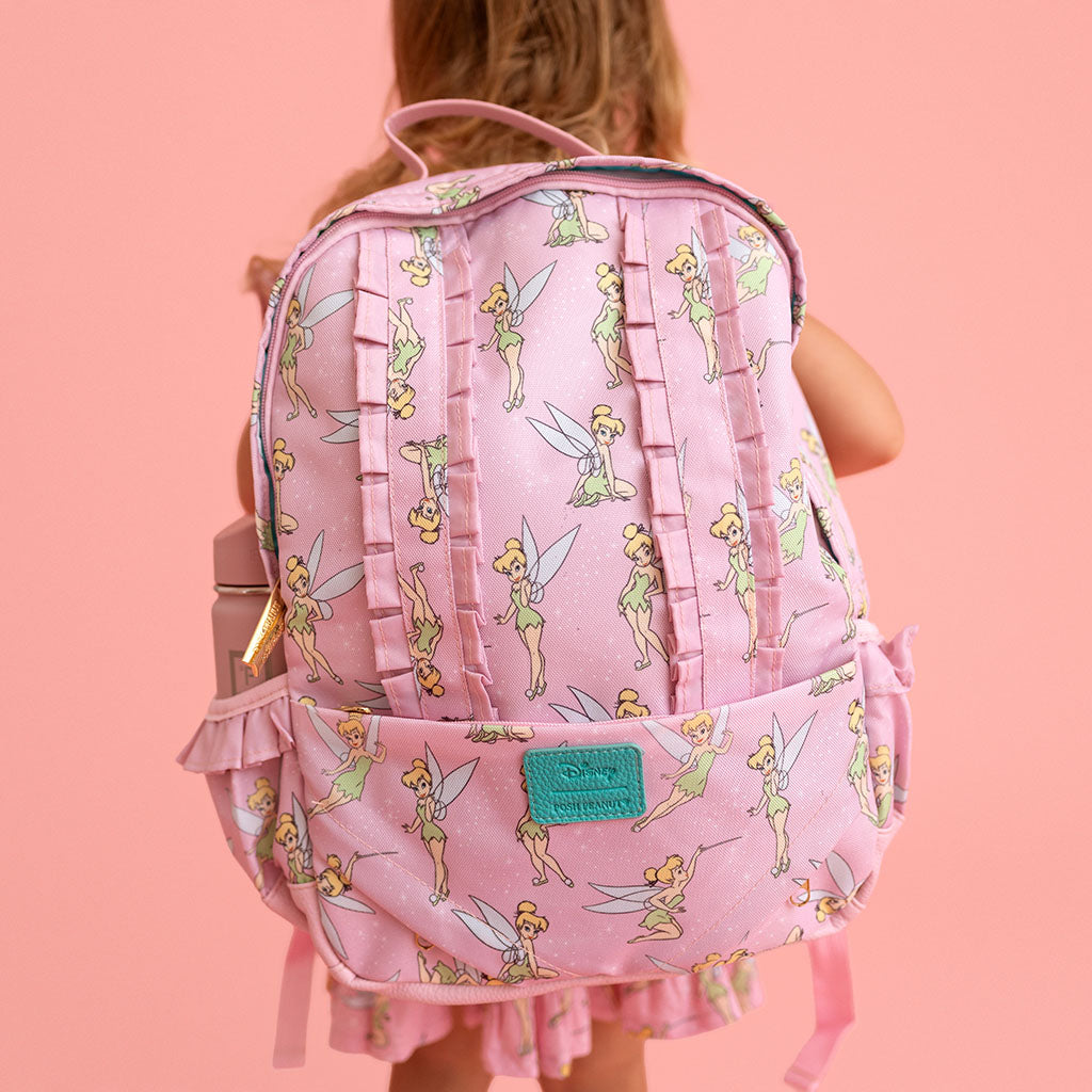 Pink backpack with fairy pattern worn by a person on a pink background