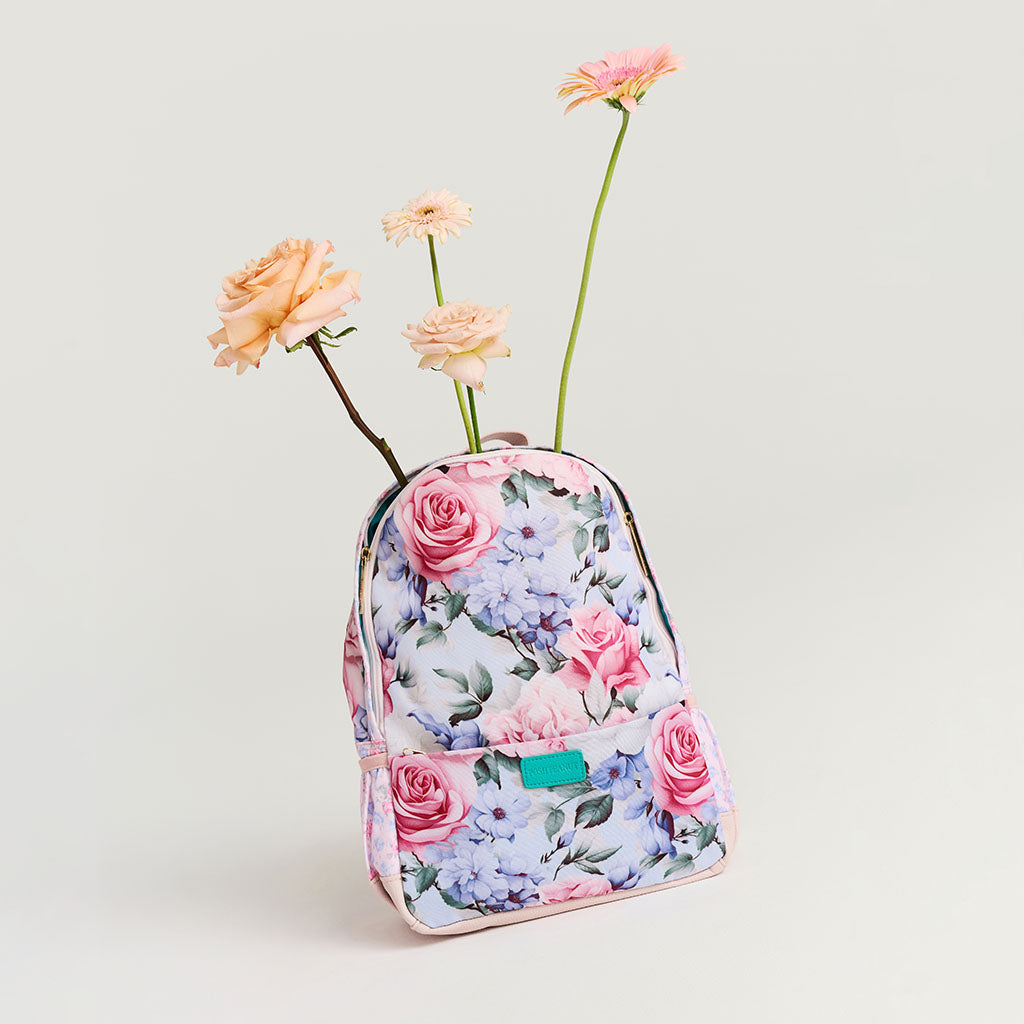Floral-patterned backpack with flowers emerging from it on a light gray background