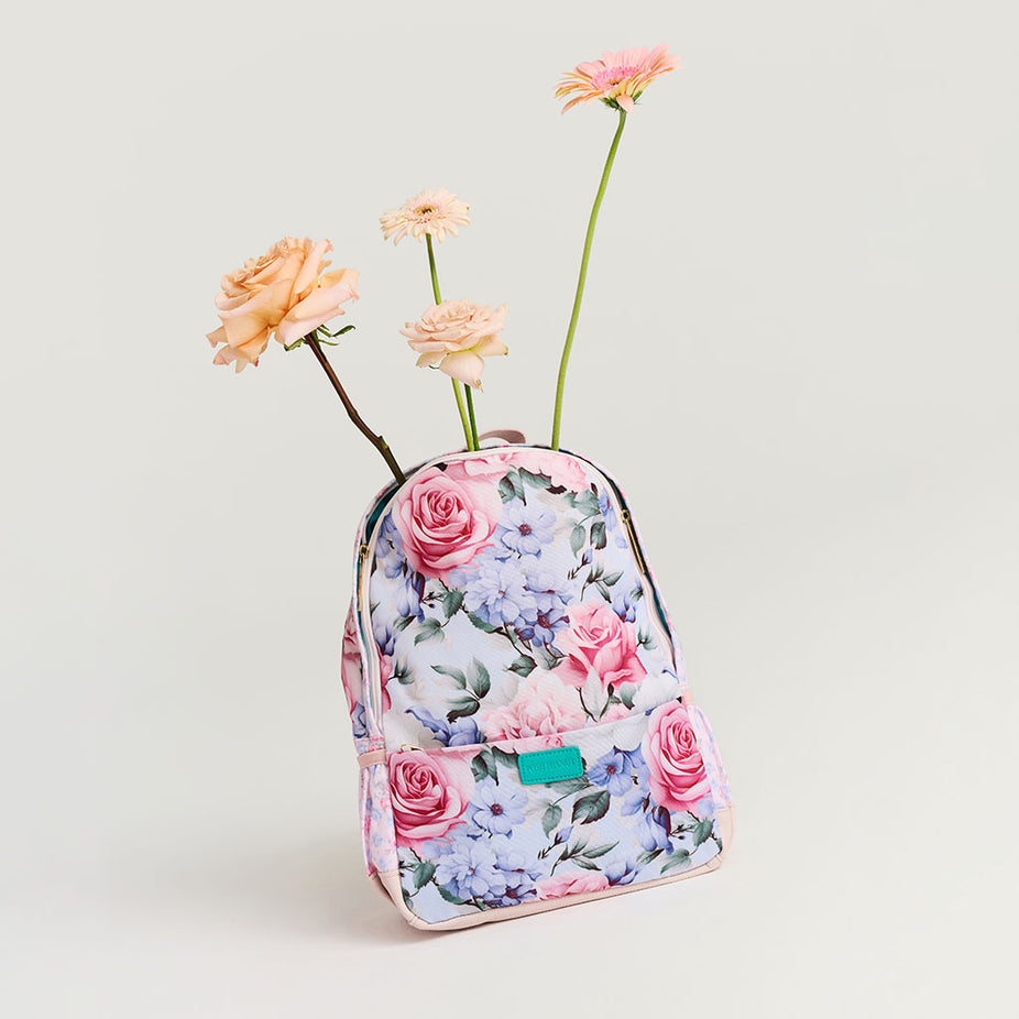 Floral-patterned backpack with flowers emerging from it on a light gray background