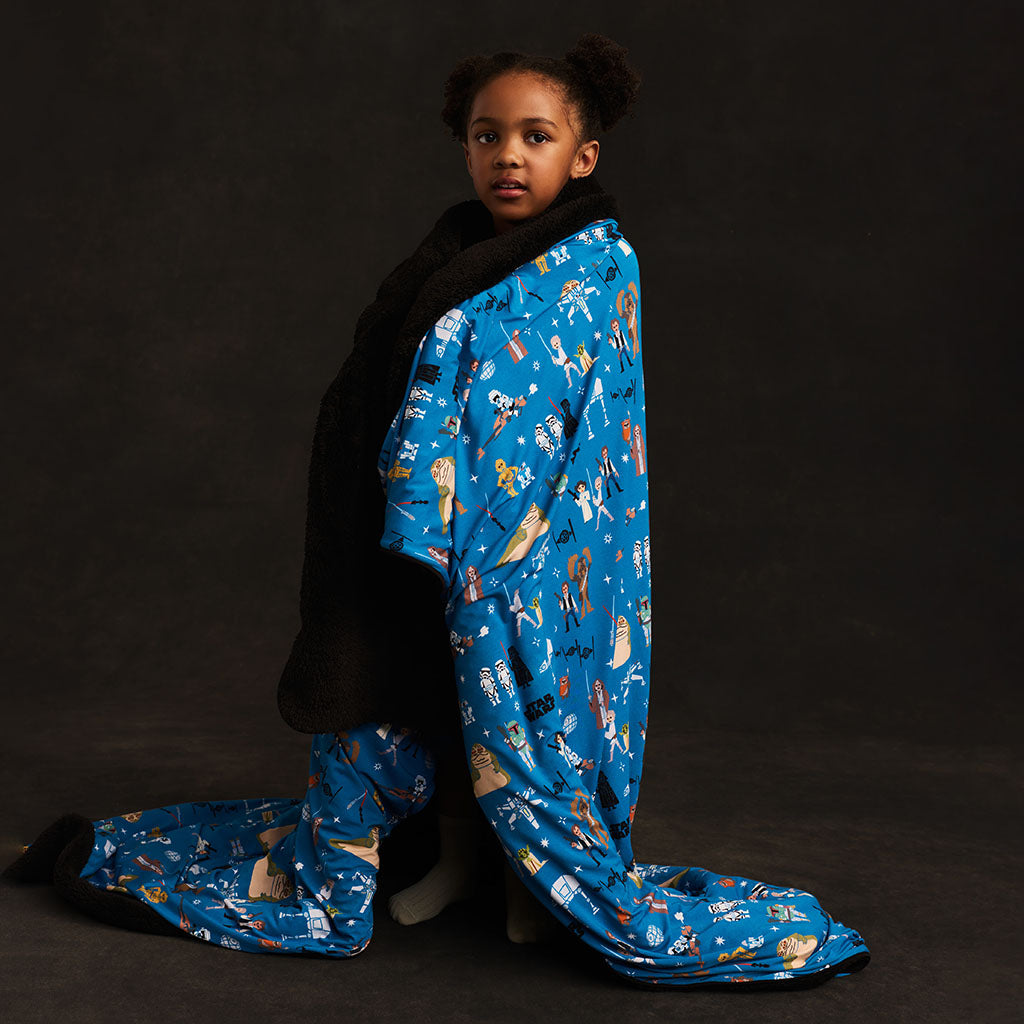 Child wrapped in a blue patterned blanket against a black background