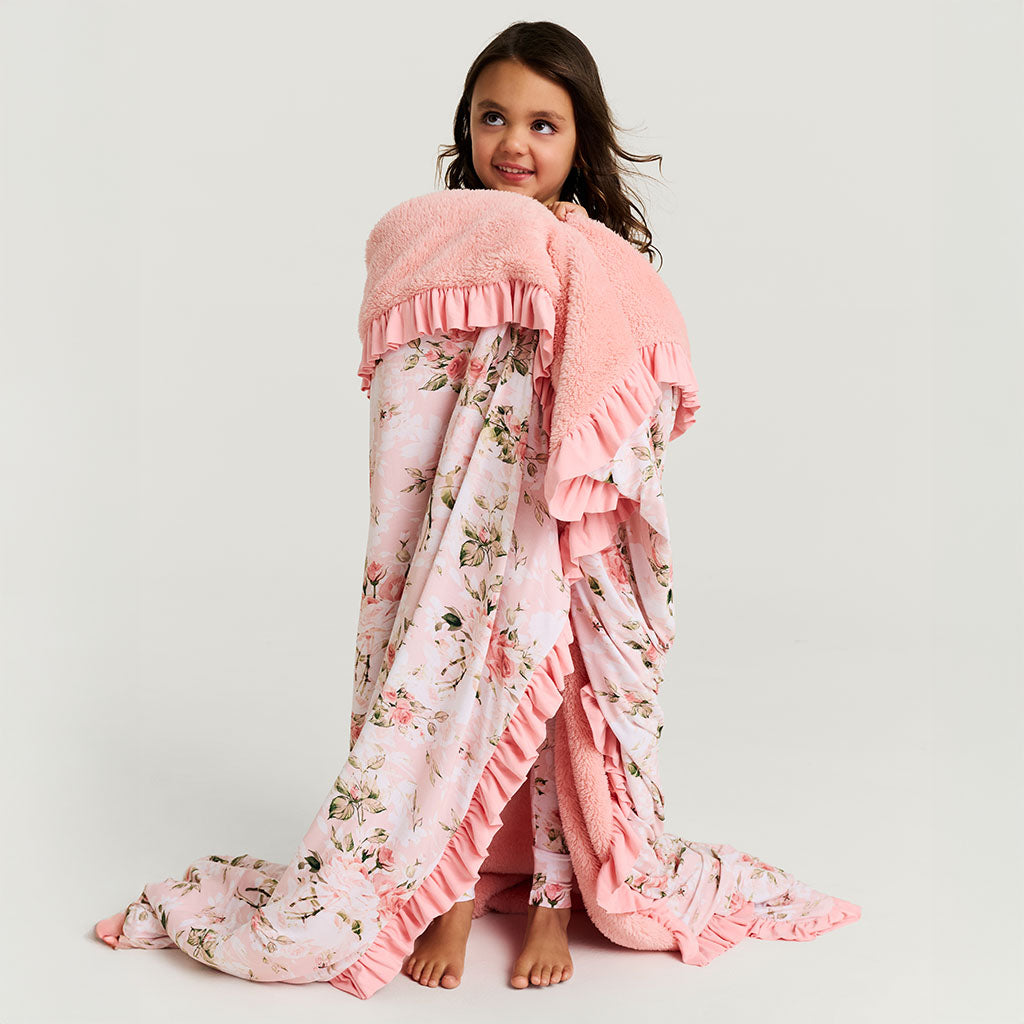 Young girl wrapped in a pink floral blanket against a white background