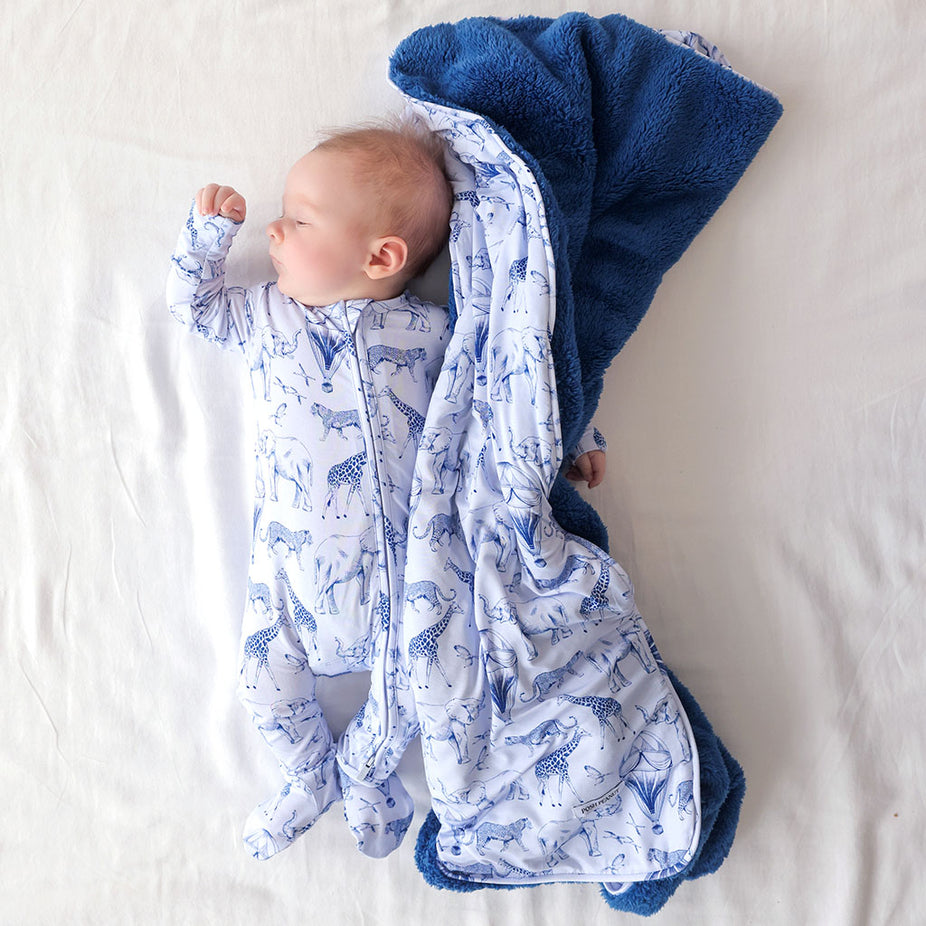 Baby wrapped in a blue and navy patterned blanket on a light background