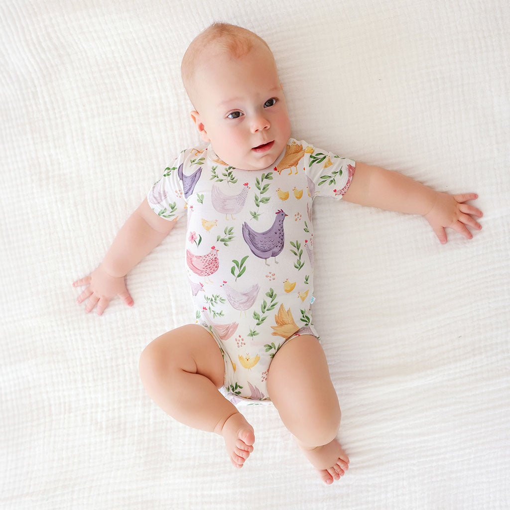 Baby wearing a colorful onesie with chicken print on a white blanket