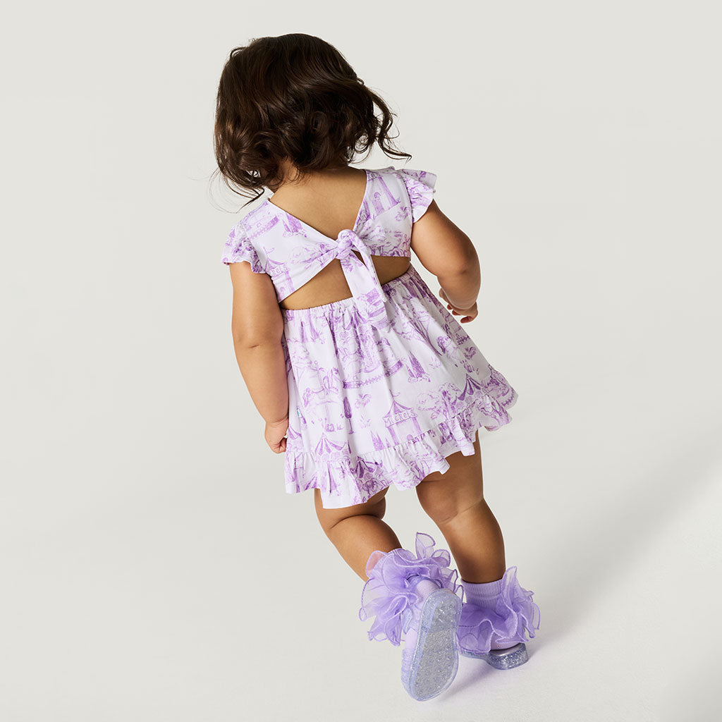 Child wearing a purple floral dress with cut-out back and matching shoes on a white background