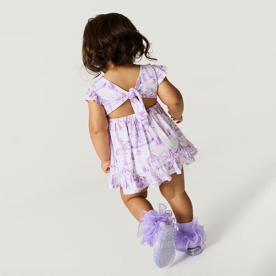Child wearing a purple floral dress with cut-out back and matching shoes on a white background