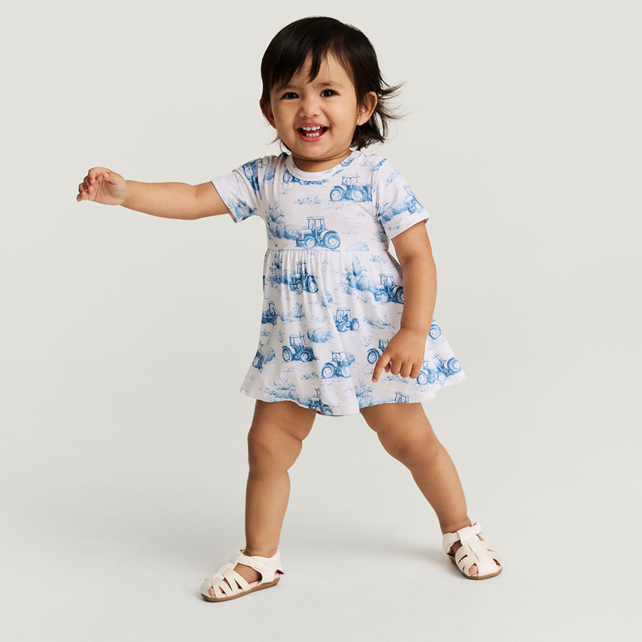 Child wearing a white dress with blue patterns on a plain background
